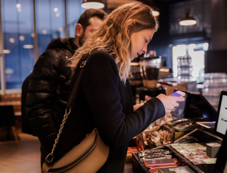 Kvinna vid kassa använder sin mobiltelefon för att betala, med en man stående bakom i kön