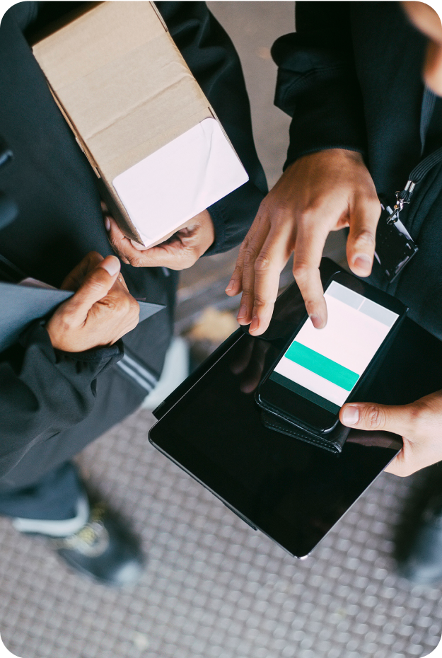 Två personer i mörka arbetskläder där en använder en mobil integrerad med Cash IT kassasystem, den andra bär ett fyrkantigt paket