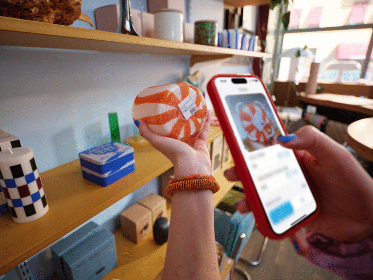 Person använder mobilen för att skanna en glasprodukt i butikshylla med självskanning och digital betalning.